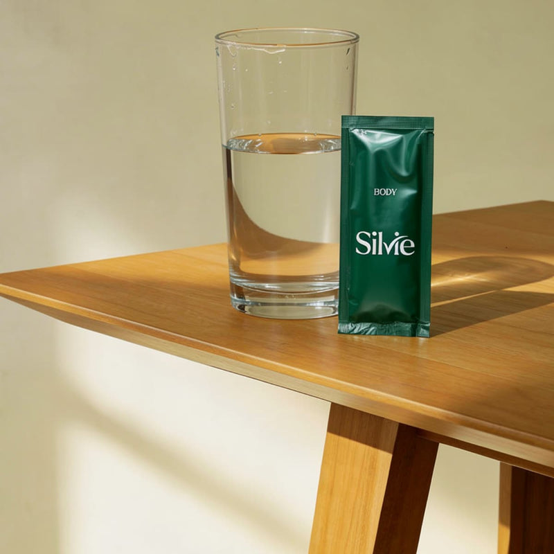 Sachet of Silvie Body next to a glass of water on a wooden table