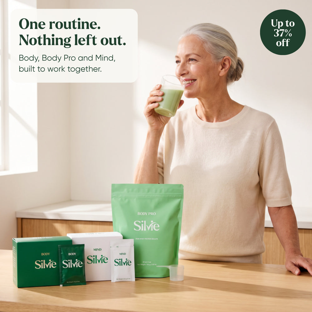 Woman in her 60s drinking her morning glass in a bright kitchen, with Silvie Body, Body Pro and Mind on the counter