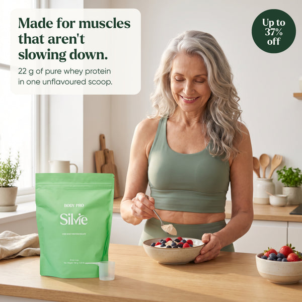 Woman in her 60s adding a scoop of Silvie Body Pro to a yoghurt bowl in a sunny kitchen, the pouch beside her