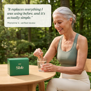 Woman in her 60s stirring a Silvie Body sachet into water on a garden terrace, with a verified customer review