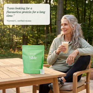 Woman in her 60s with a protein drink on a forest terrace, Silvie Body Pro pouch on the table, with a customer review