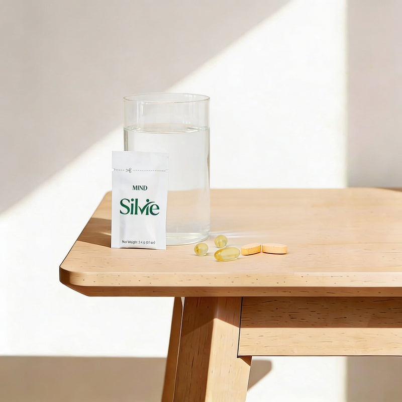 Silvie supplement packaging on a wooden table with a glass of water and pills.