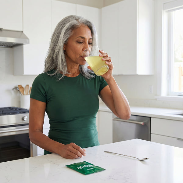 Woman drinking Silvie Body with a glass of water in a kitchen